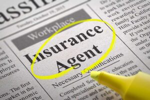 A couple reviews auto and home insurance policy documents beside a laptop and calculator at a kitchen table.