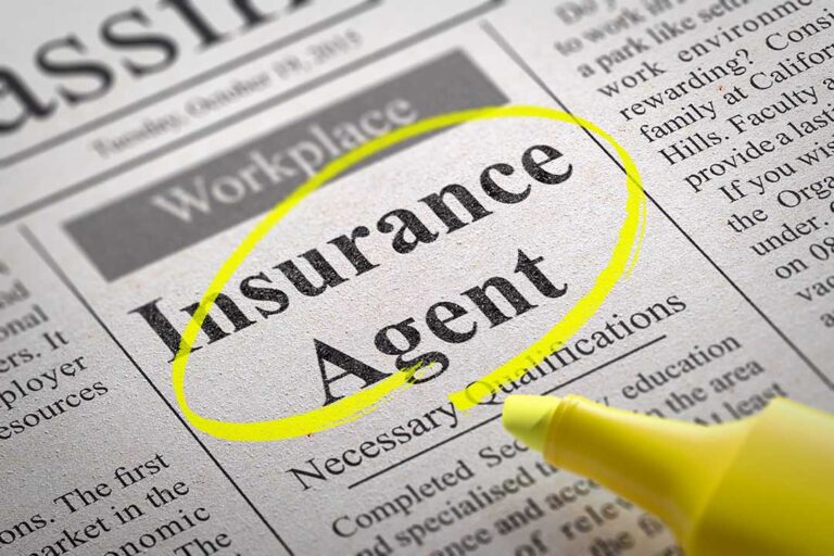 A couple reviews auto and home insurance policy documents beside a laptop and calculator at a kitchen table.